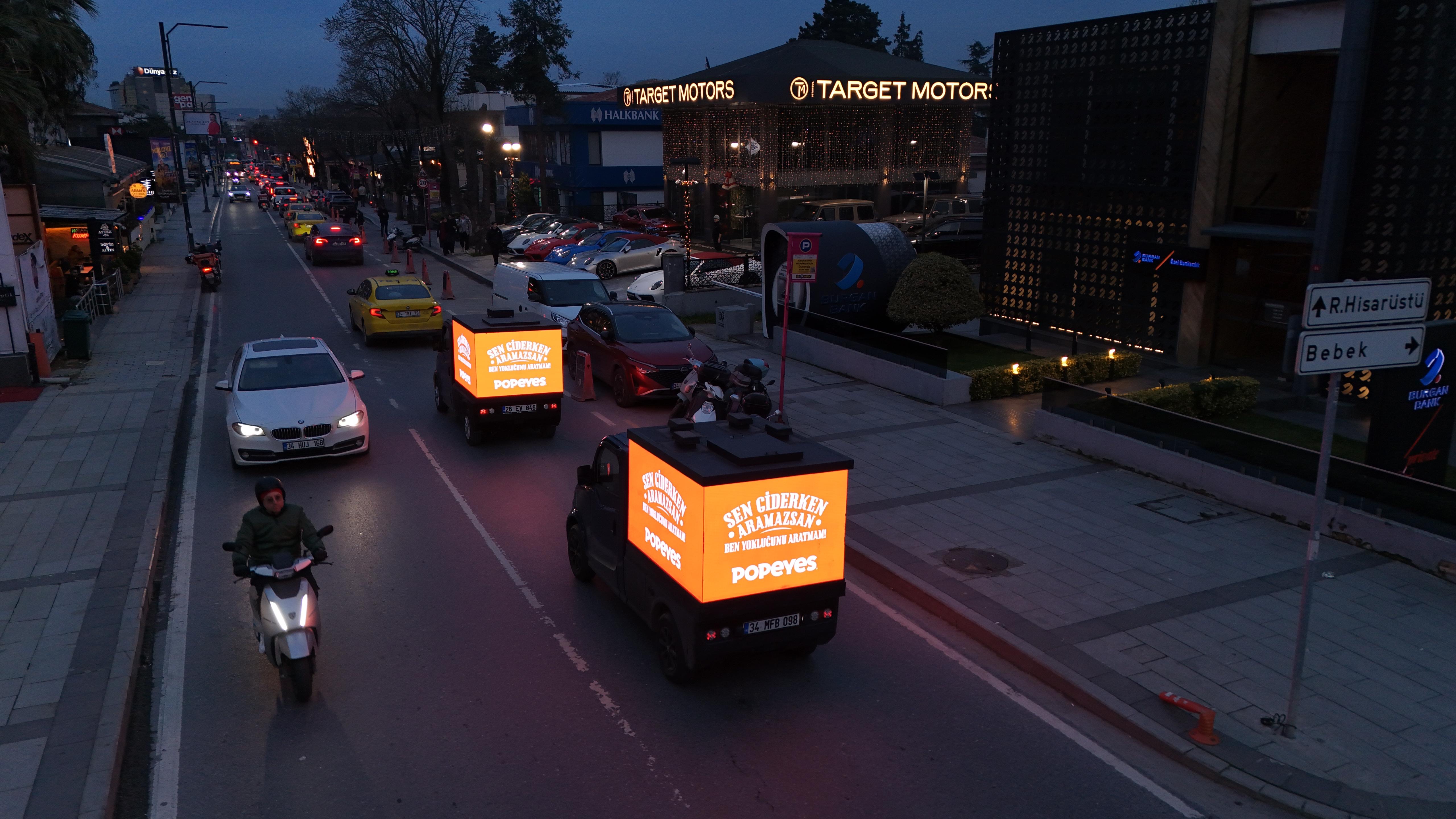 Akşam trafiğinde Popeyes reklamı gösteren iki VIOR aracı
