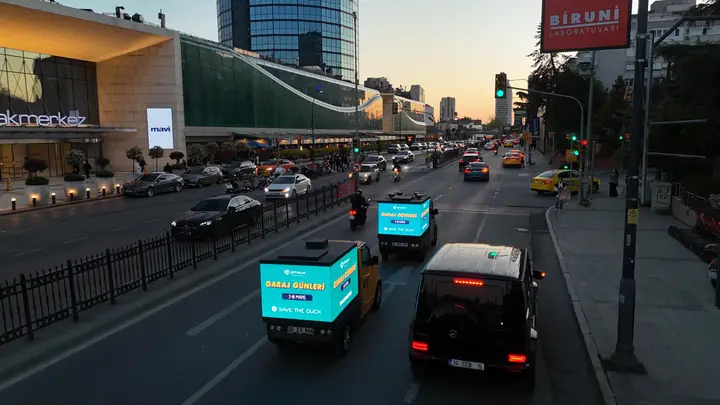 Akmerkez önünde gün batımında LED ekranlı araçlar